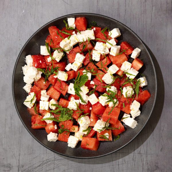 Overhead view of a Watermelon Feta Mint Salad on a round black plate over a gray wood table surface.