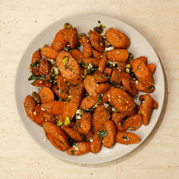 Overhead view of roasted herb feta & carrots on a round white plate over a natural linen tablecloth.